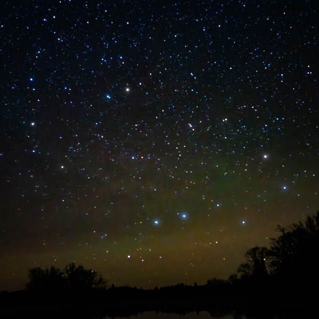 A landscape photo of many stars illuminating the night sky and reflecting onto the river.