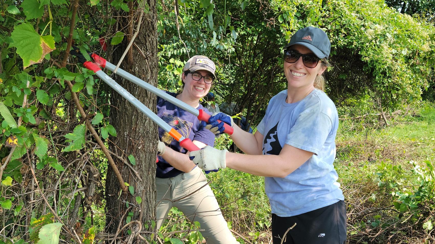 Two people standing with loppers by a tree.