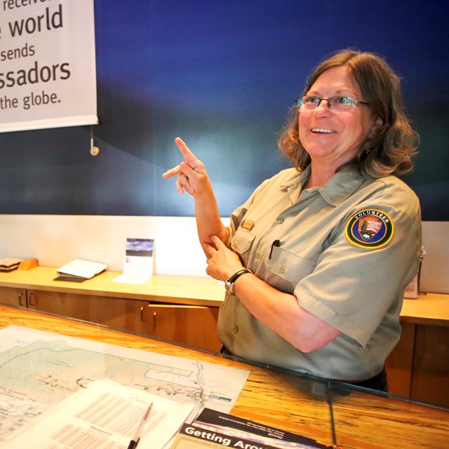 A person in an NPS volunteer uniform makes the letter K in American Sign Language with their hands.