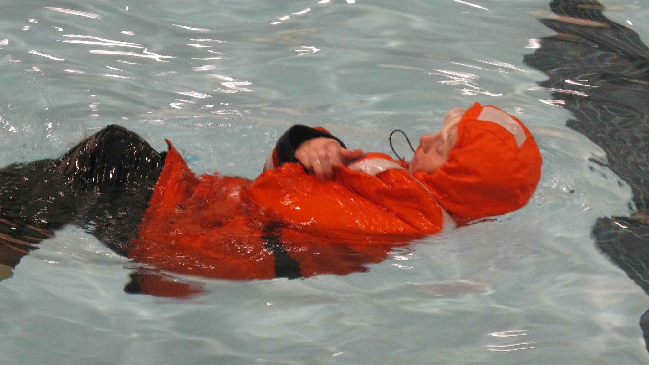 A person in an orange survival suit floats in the water. 