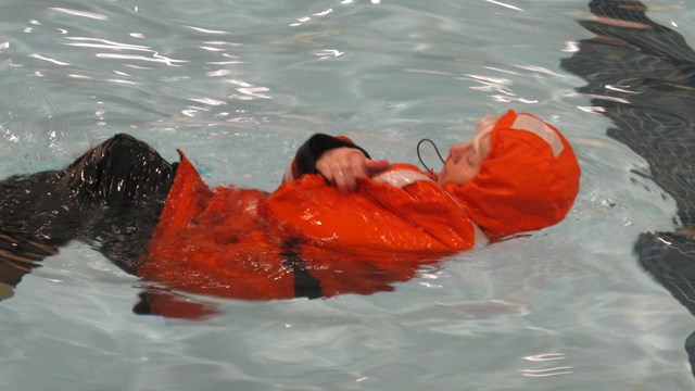 A person in an orange survival suit floats in the water. 