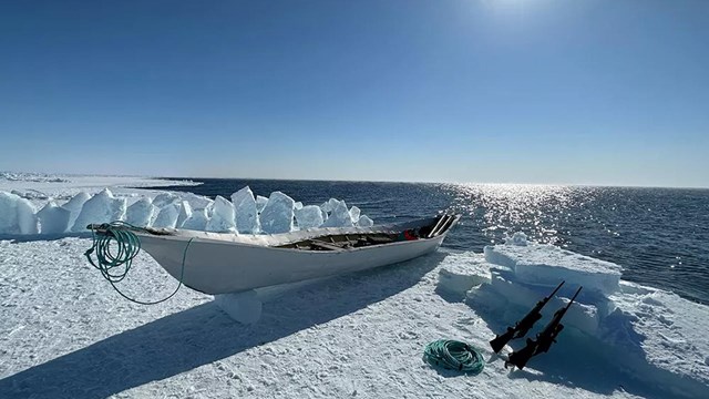 A boat and two rifles on ice along the water