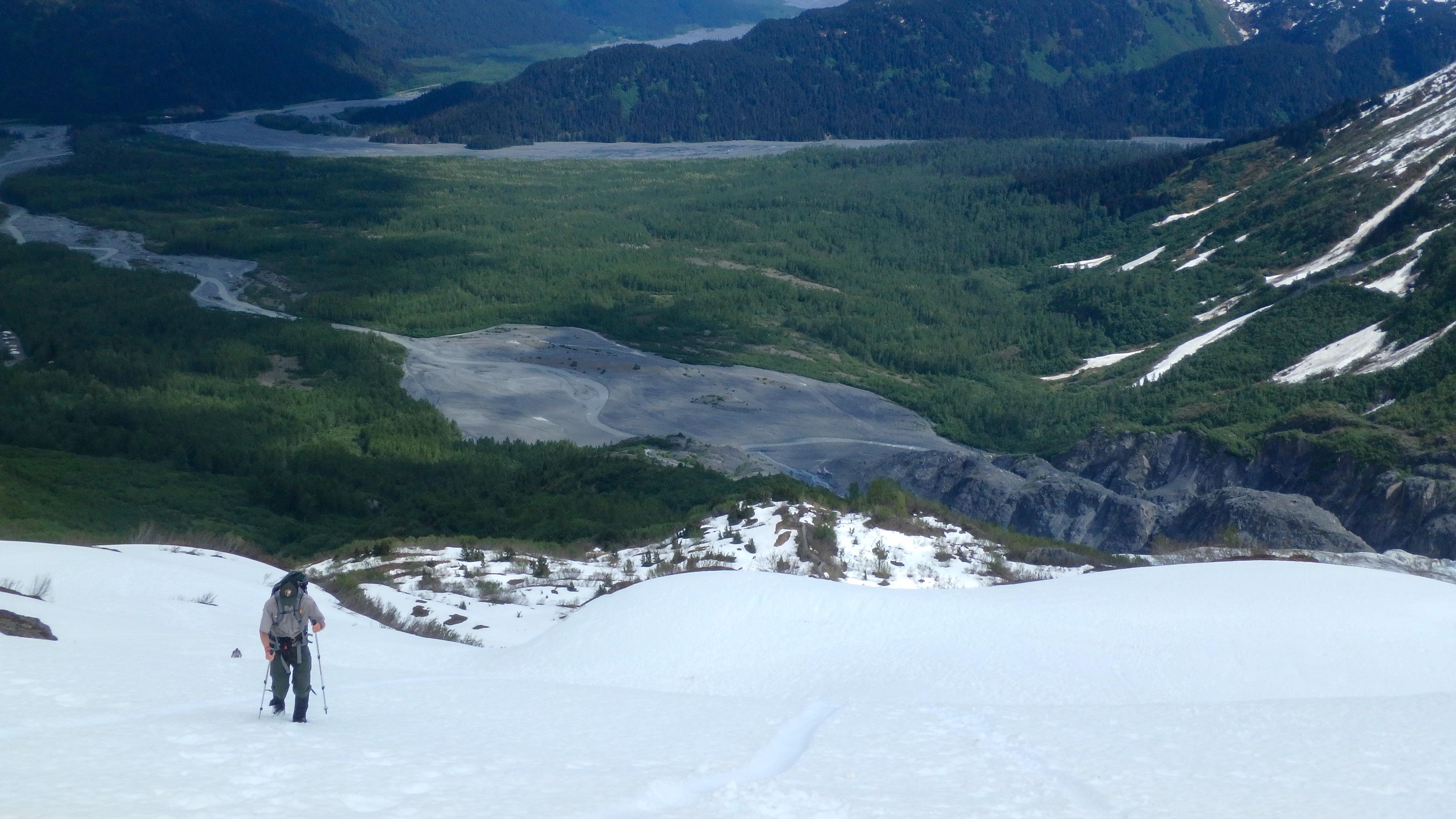 A ranger hikes on snowy terrain with a valley below