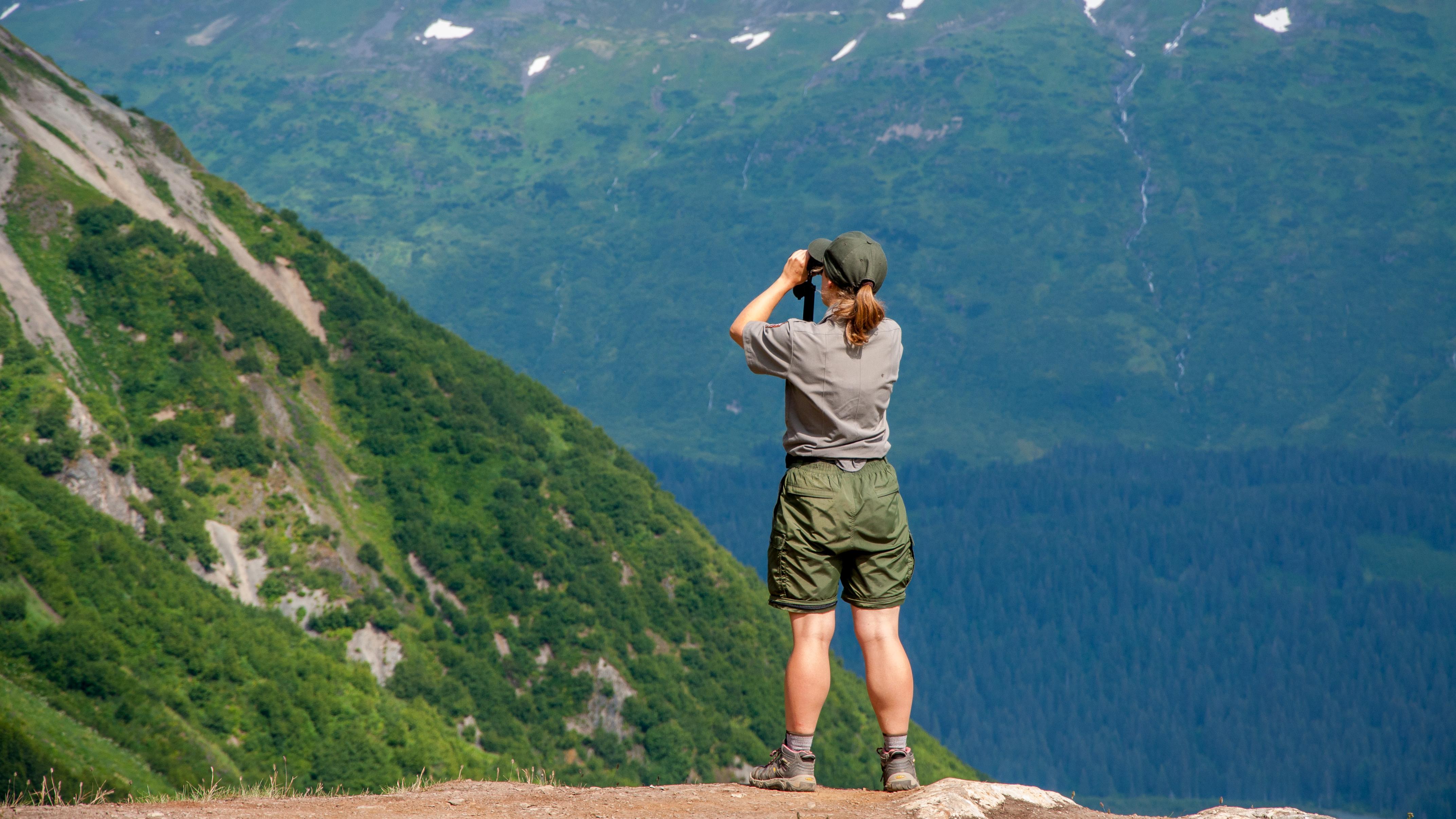 A park ranger looks out at the distance through binoculars
