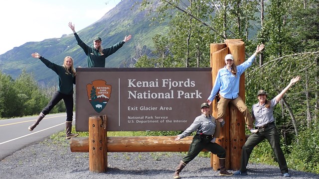 Five staff pose along with the Kenai Fjords National Park road-side sign.