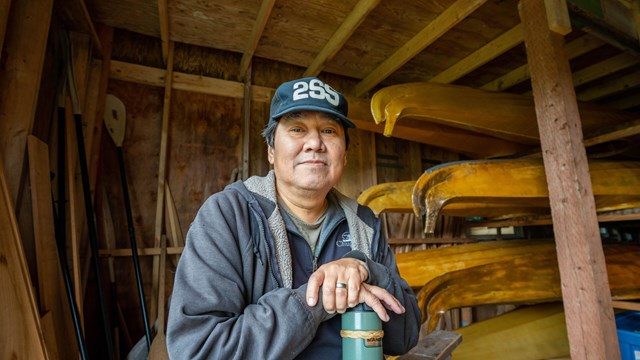 A person poses with traditional qayaqs (kayaks) in the background