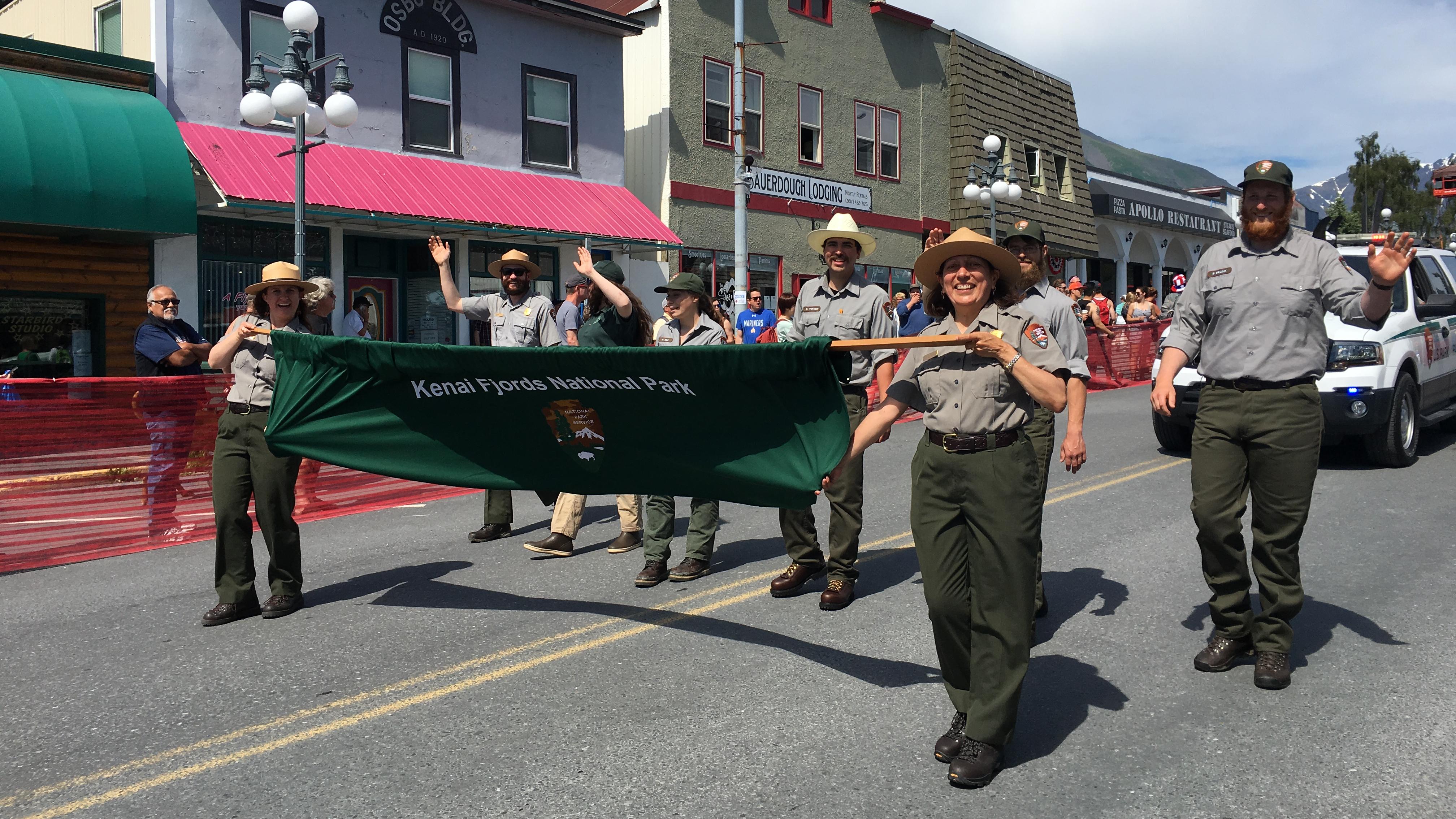 Park rangers walk in a parade with a Kenai Fjords National Park banner.