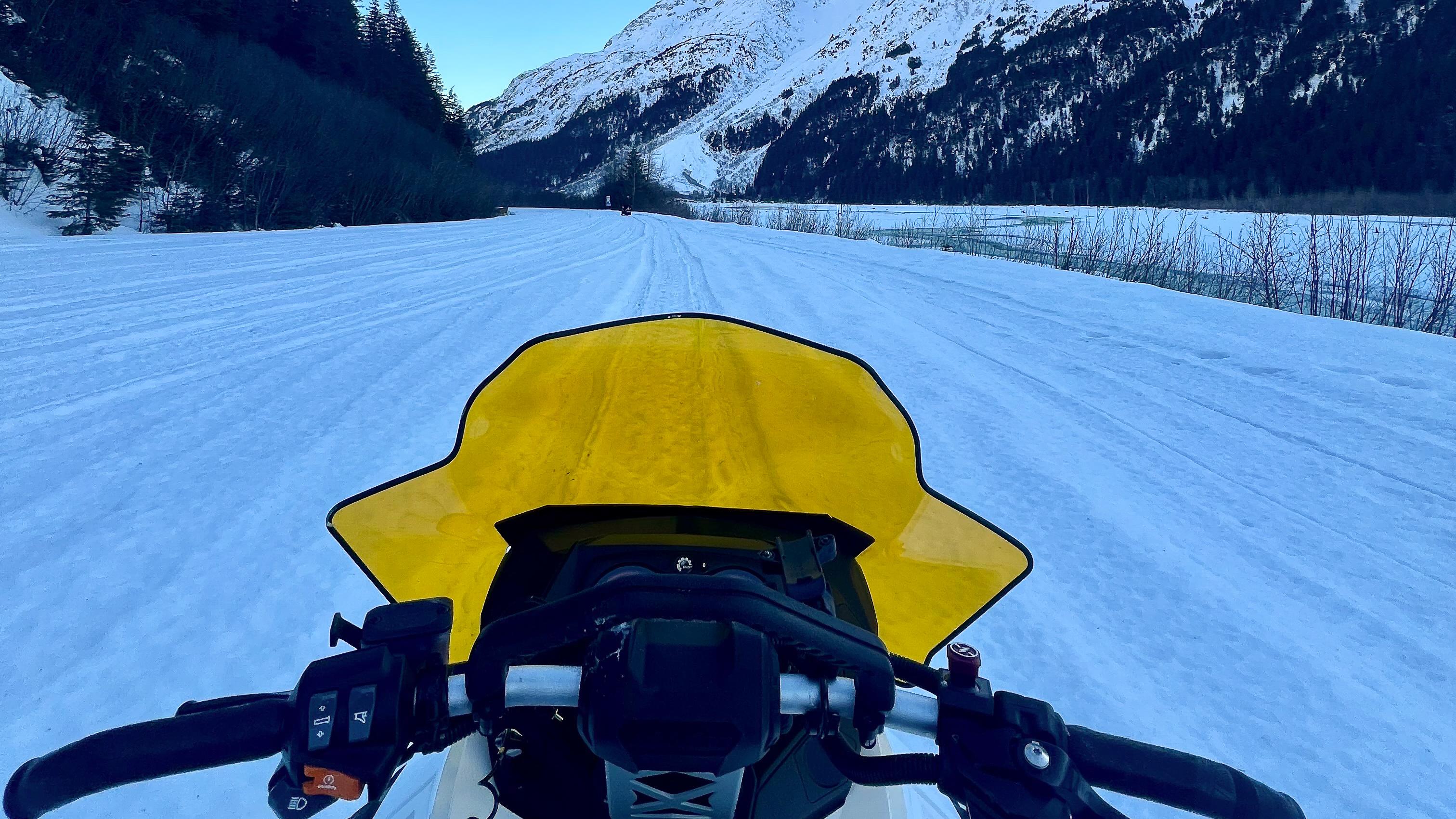 A snow covered road from perspective of snowmobile rider