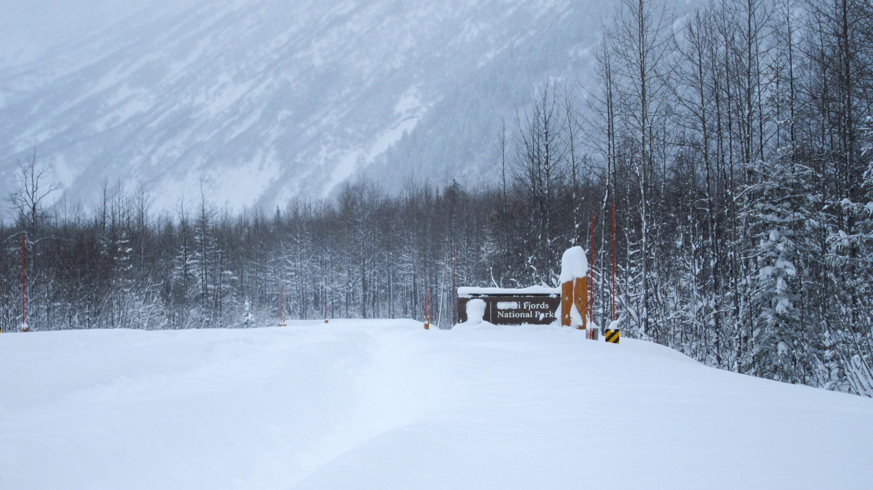 A snow-covered road with the Kenai Fjords National Park sign sticking out