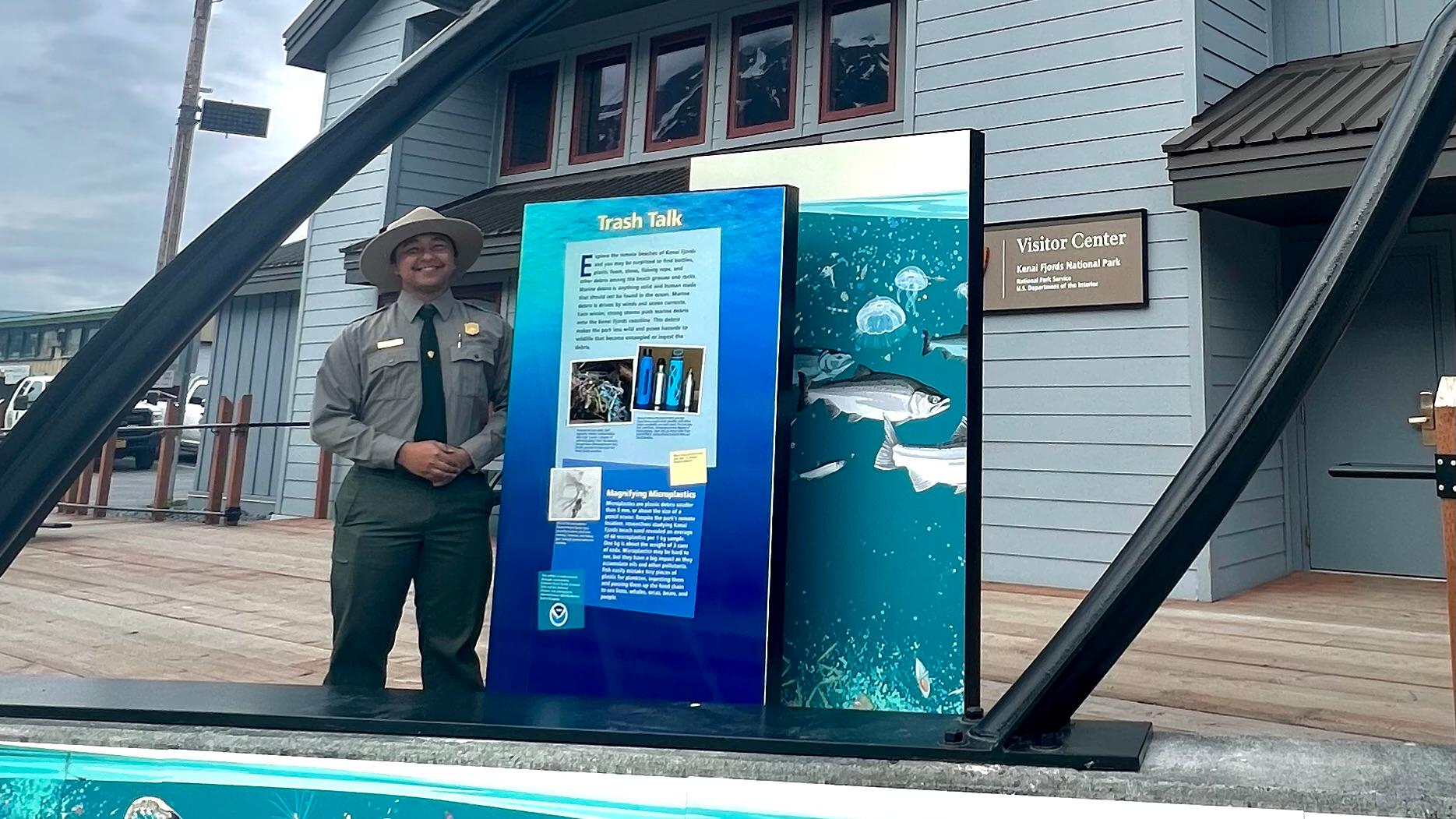 A ranger poses with a interpretive panel and whale sculpture