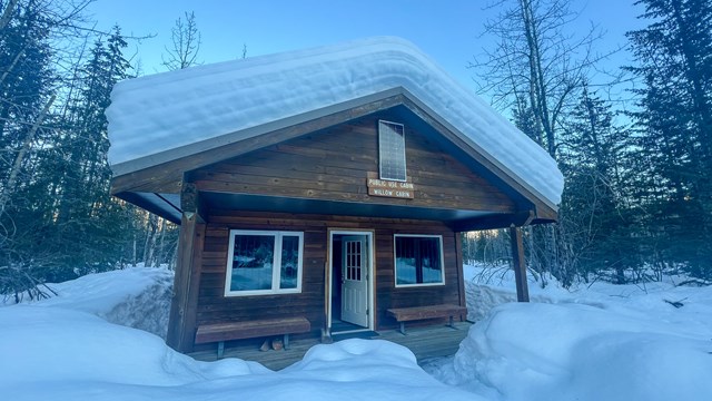 A cabin covered and surrounded by snow.