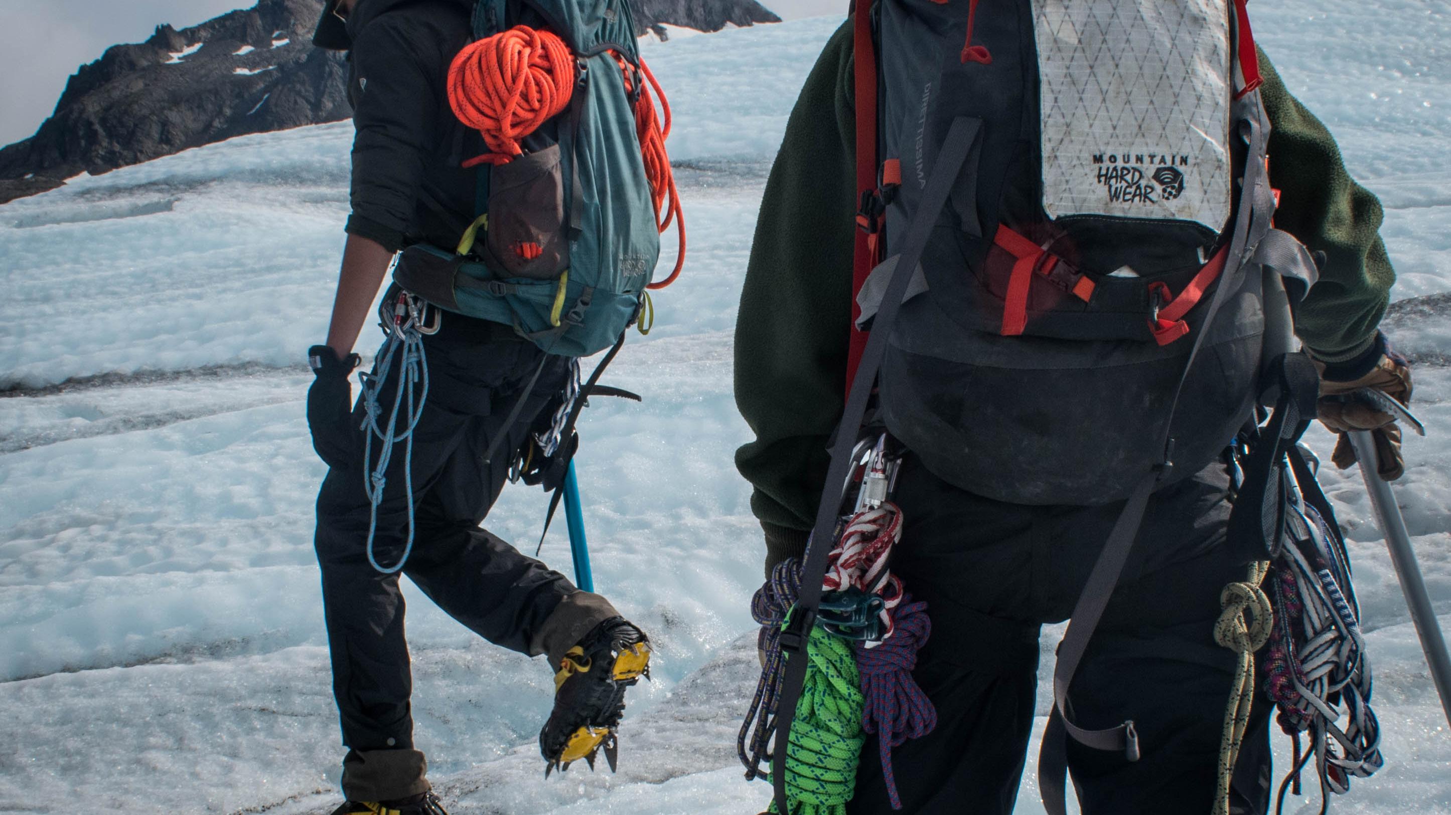 Two people with ice climbing gear walk on glacial ice