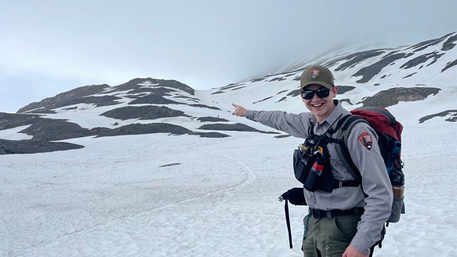 A park ranger points to a safety hut on a snowy hill in the distance