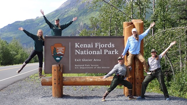 Five people in different uniforms pose with the Kenai Fjords National Park sign