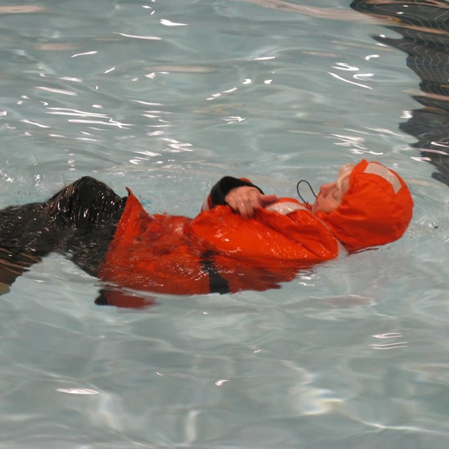 A person in an orange survival suit floats in the water. 