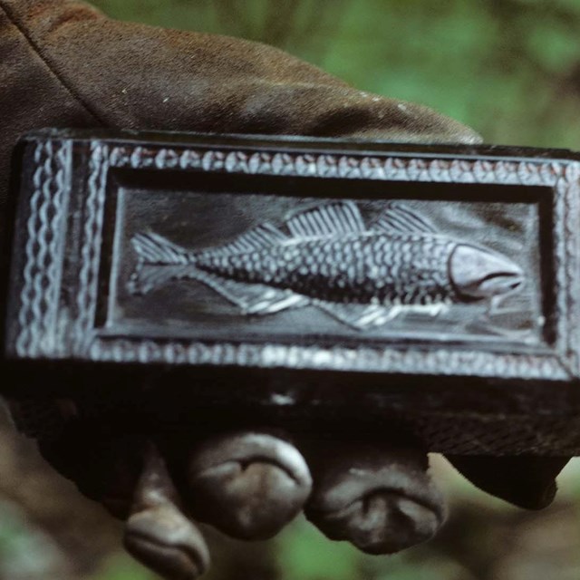 A hand holds a bottle with an embossed fish. 