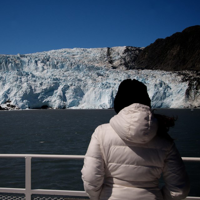 A woman looks at a tidewater glacier from the rail of a tour boat.