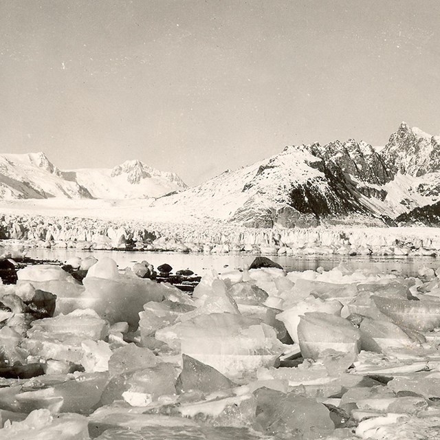 A black and white photo.  Chunks of ice are in the foreground of the image. d