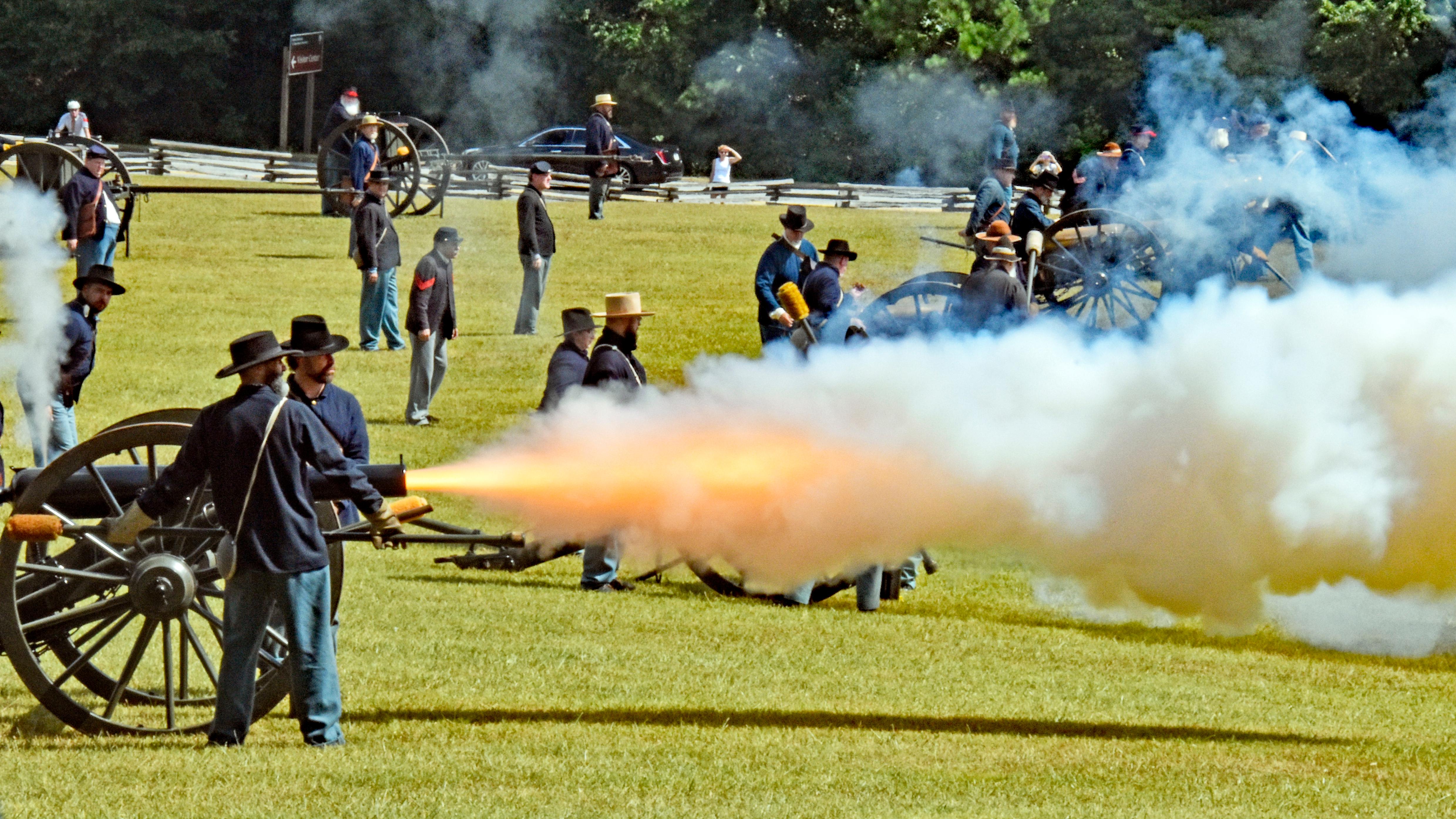 Cannon crew firing cannon in grassy field. Smoke and fire come out of cannon.