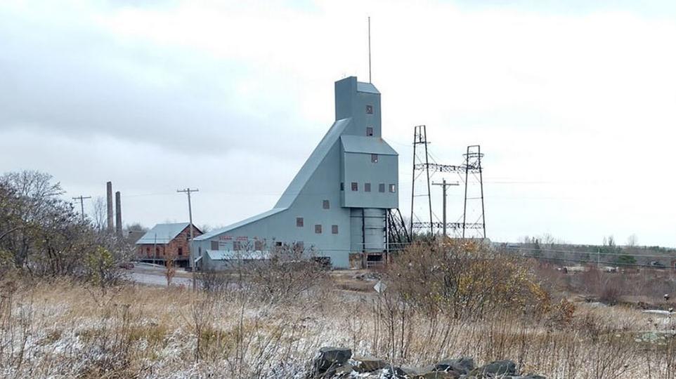 Fall image of a barren former industrial landscape with a tall silver building in the background.