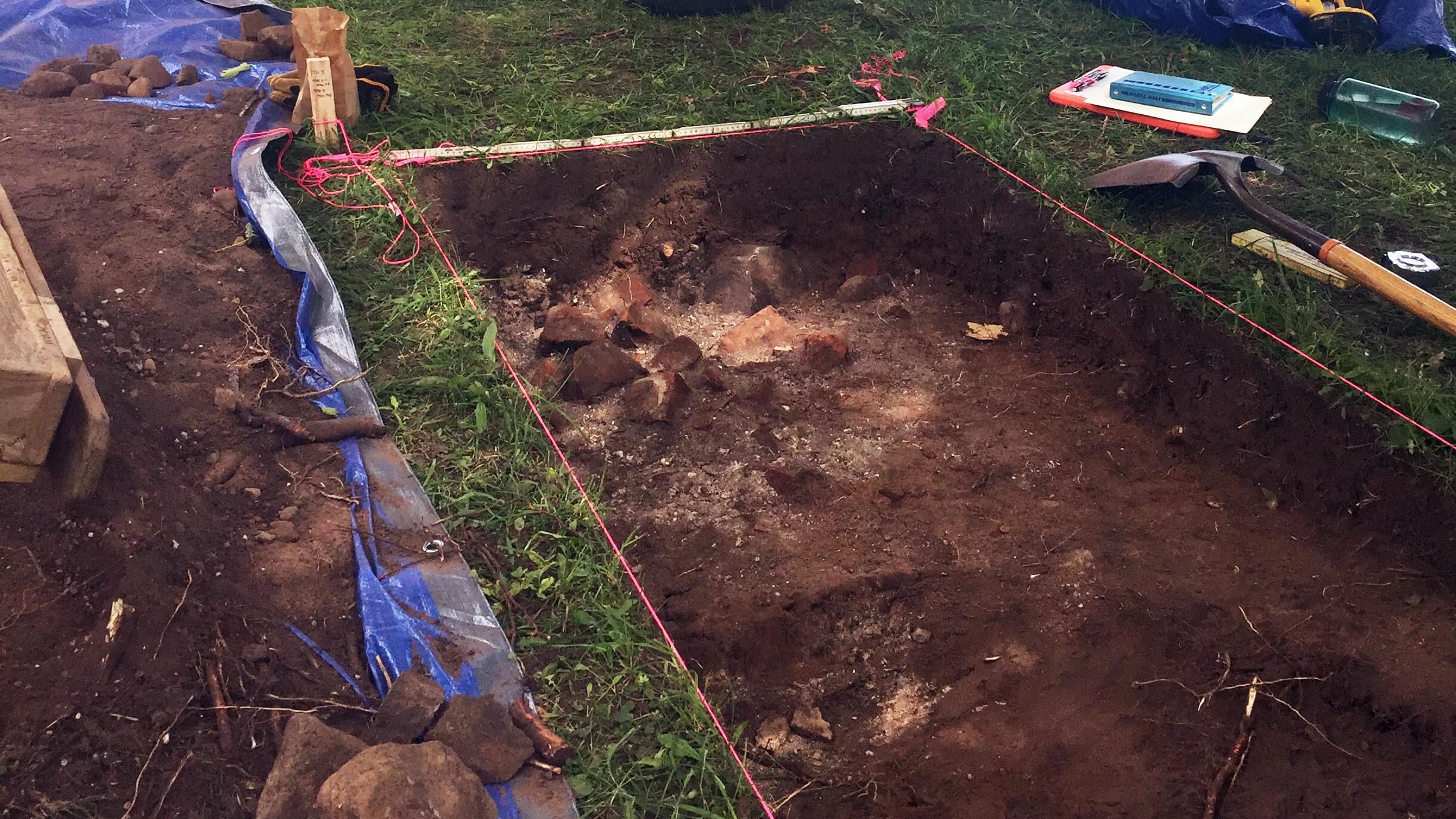 A large rectangular hole in the ground surrounded by tools.
