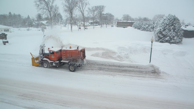 A snow-go machine removes snow along a street.