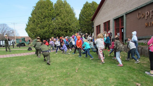 A large group of students use their bodies to mimic adult leaders.