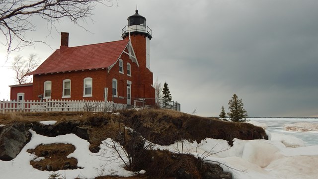 A brick lighthouse along a rocky shoreline covered in ice and snow.