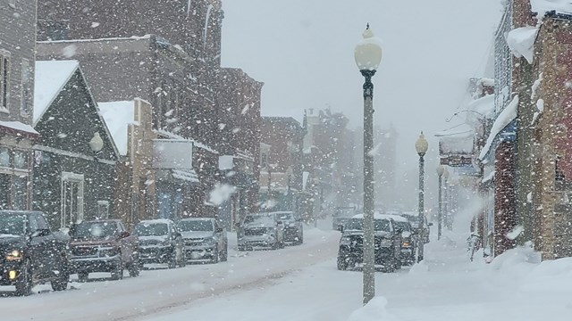 A busy main street lined with buildings while heavy snow falls.