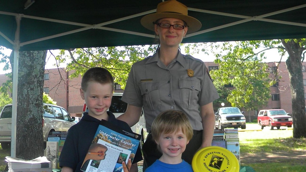 A park ranger poses with two junior rangers
