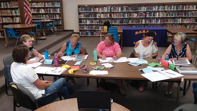 A group of people sits around a table talking and writing on paper.