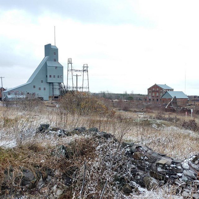 Fall image of a barren former industrial landscape with a tall silver building in the background.