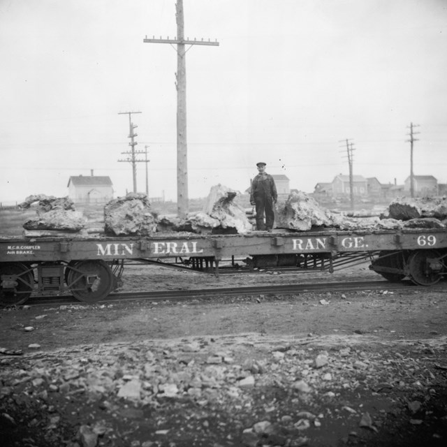 Image shows a man standing on flat bed rail car with a load of copper
