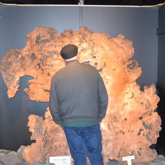 A man with back to camera stands in front of a float copper sample bigger than him.