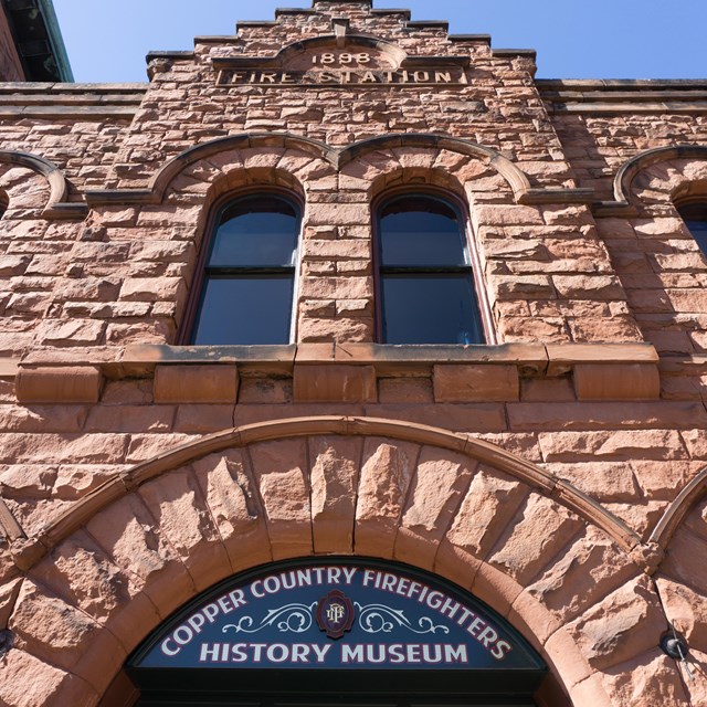 Looking upward at a brown stone, 2 story building. Blue sky is up above.