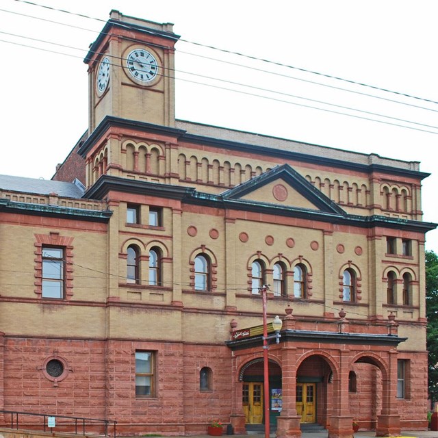 A large red, sandstone and cream-colored brick building sits on a historic corner.