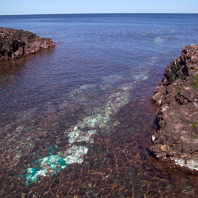 Rocks protrude up out of a lake, with a green copper vein extending out underwater.