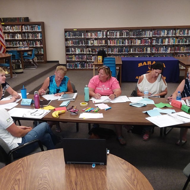 A group of people sit around a table talking and writing on paper.