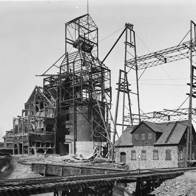 Black and white historic image showing a tall metal building being built, with steel supports.