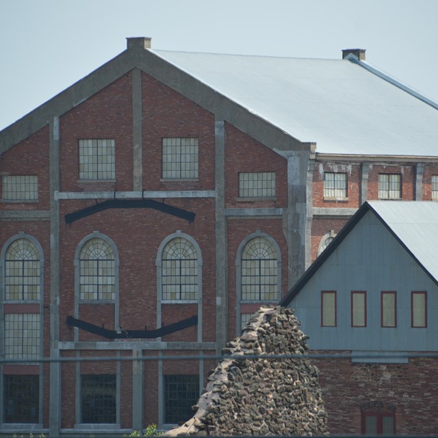 A large red brick and concrete building on the left and smaller red stone and building on the right 