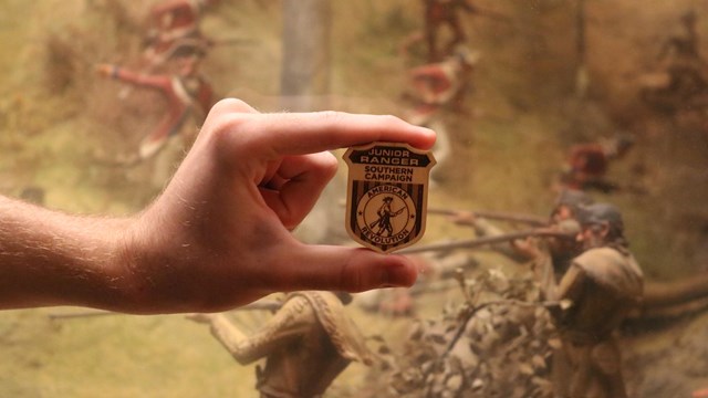 A hand holding a wooden badge with Southern Campaign and Junior Ranger on it