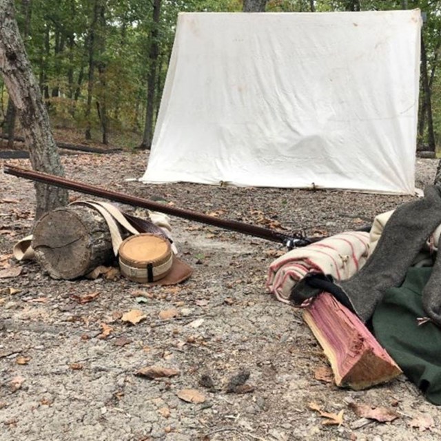 A white tent and some camping gear on the forest floor.