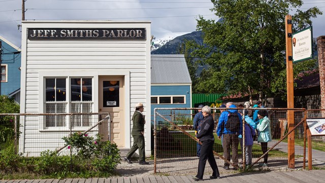 A ranger walks towards people in front of a small, white building