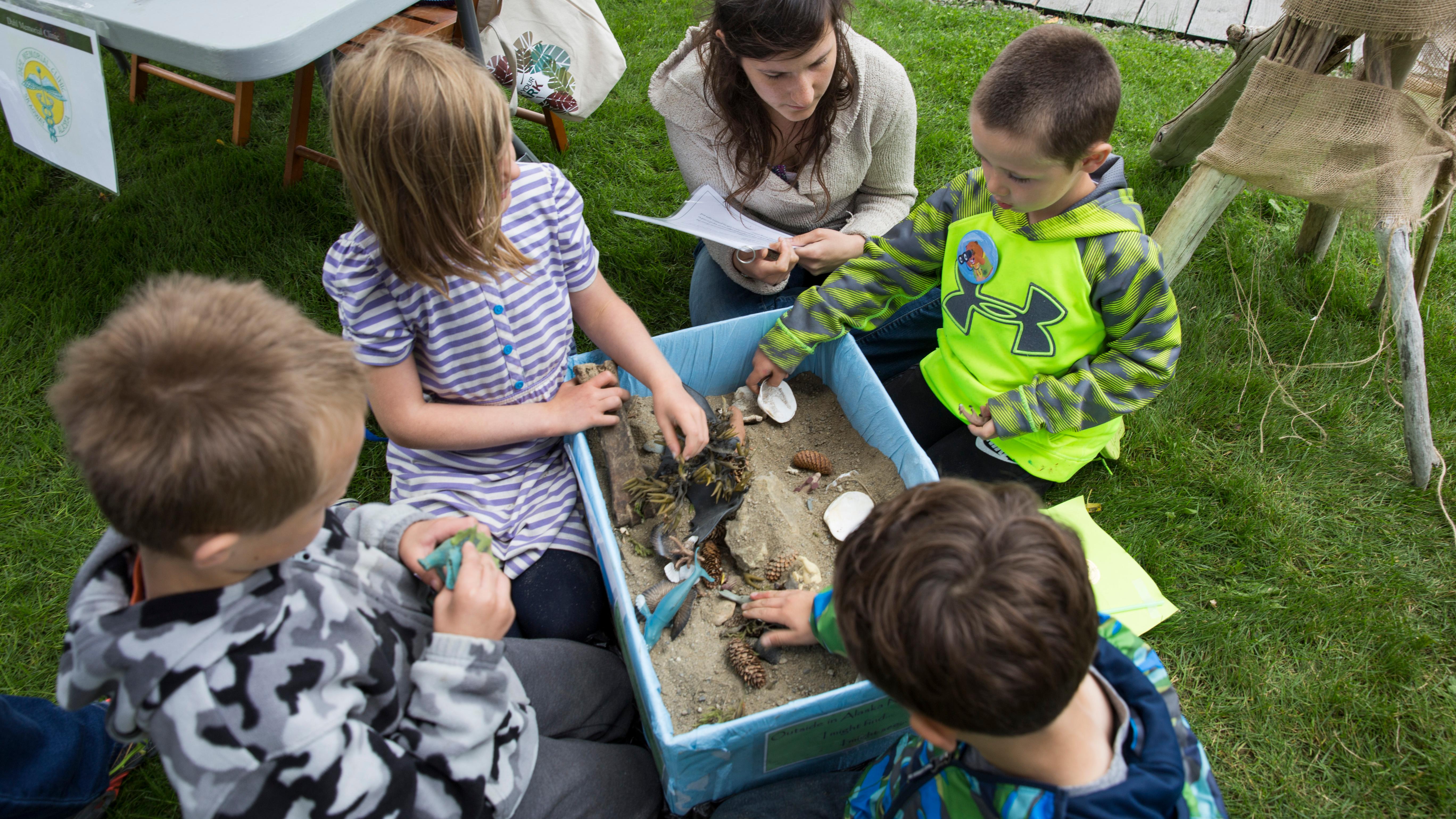 Kids gather around a container with sand and objects.