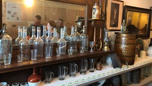 Bottles, glasses, and other items line an old back bar with a mirror behind them