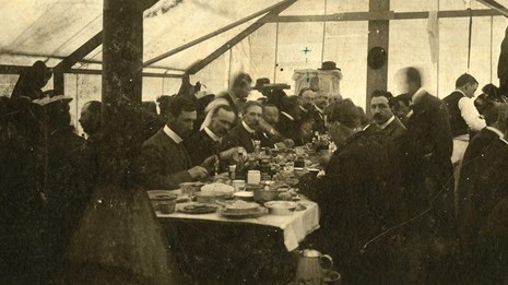 people sit at a long table inside a dining tent
