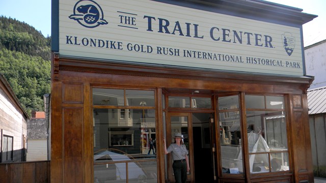A ranger poses in the door of a building with large windows and a sign reading "The Trail Center"