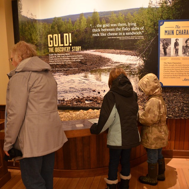 An adult and two children look at an exhibit about gold discovery