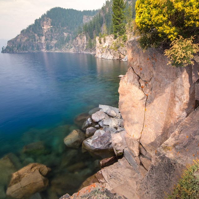 View of Crater Lake shore with boulders and shrubs in foreground