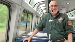 Smiling volunteer guide on board an train wearing green uniform and headset. 